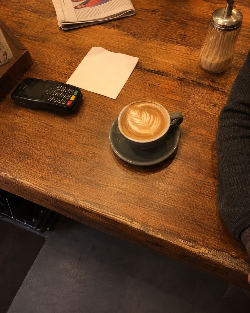 The photograph most cafés take: a flat white on a table shot from standing height under warm downlights, a card machine and somebody's elbow in the frame.