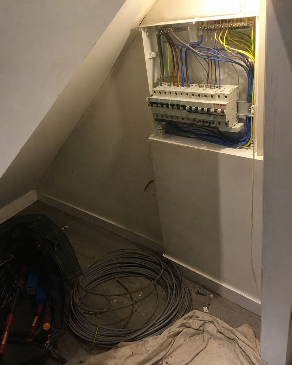 The photograph most electricians take: a newly fitted consumer unit shot in a dim cupboard at an angle, cable offcuts on the floor beneath it.