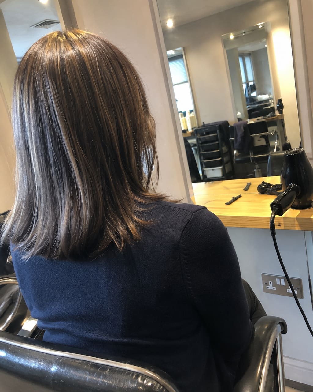 The photograph most salons take: a finished cut shot from behind at the backwash, mirrors and a trolley in the frame, overhead spots throwing a shadow down the client's face.