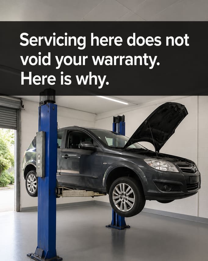 The same car on the same ramp, kept exactly as photographed, with the workshop around it replaced by a clean, bright, well-ordered bay, and the words “Servicing here does not void your warranty. Here is why” on a black band across the upper half.